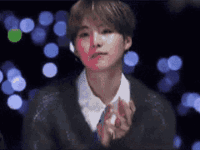 a man in a black sweater and tie is clapping his hands in front of a blurry background .