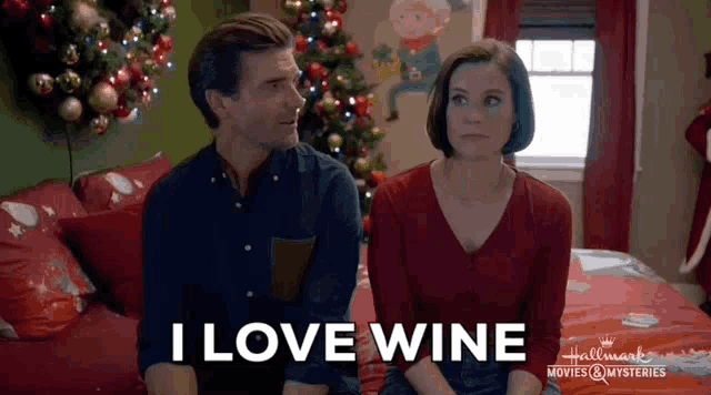 a man and a woman are sitting on a bed and the man is saying i love wine