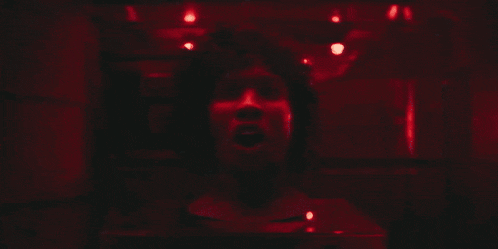 a woman in a black suit is walking through a door in a dark room