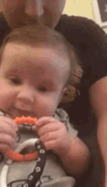 a man is holding a baby who is chewing on a teething toy .