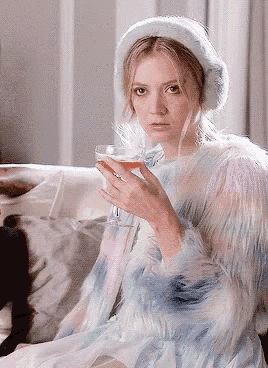 a woman in a fur coat holds a glass of wine