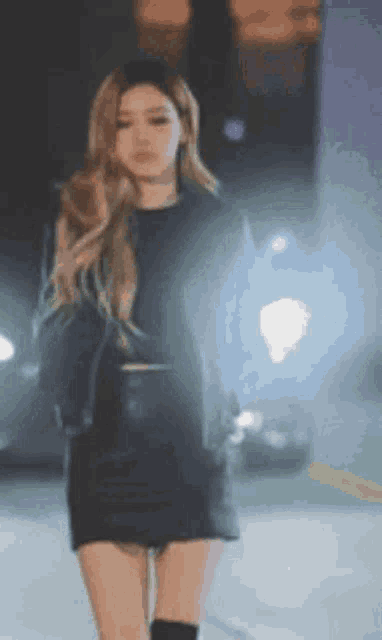 a woman in a black dress is walking down a street at night .