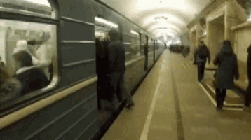a train is pulling into a subway station with people getting on and off .