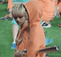 a man in an orange hoodie is standing in the grass holding a trophy .