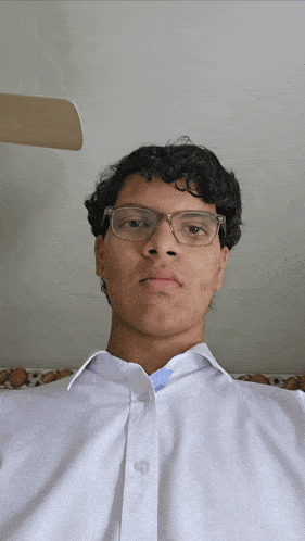a young man wearing glasses and a white shirt is sitting in front of a ceiling fan