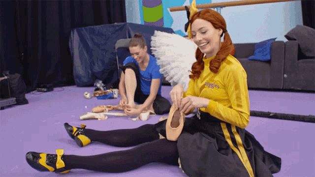 a woman in a yellow shirt that says wiggle is sitting on the floor