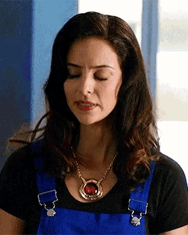 a woman wearing blue overalls and a necklace with a red stone on it