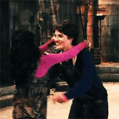 a man in a black suit is hugging a woman in a pink top