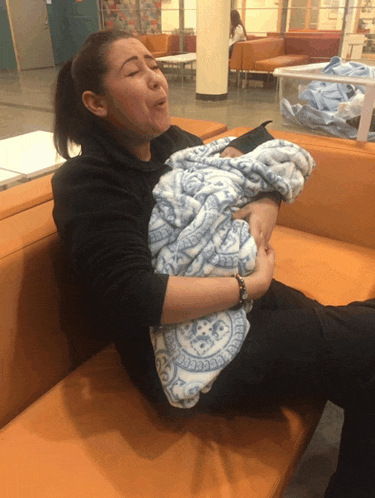 a woman sitting on a couch holding a baby wrapped in a blue blanket