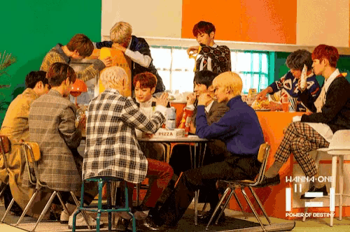 a group of young men sitting around a table with a pizza box in the background