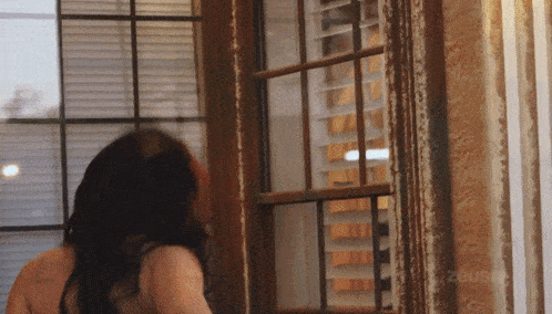 a woman standing in front of a window with the word zous on the bottom right corner