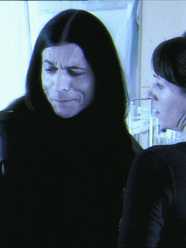 a woman with long black hair is looking at another woman