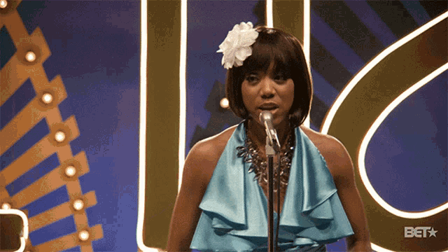 a woman in a blue dress singing into a microphone with the bet logo behind her