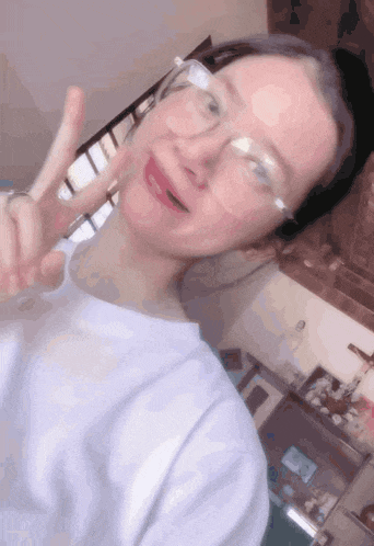 a woman wearing glasses and a white shirt giving a peace sign