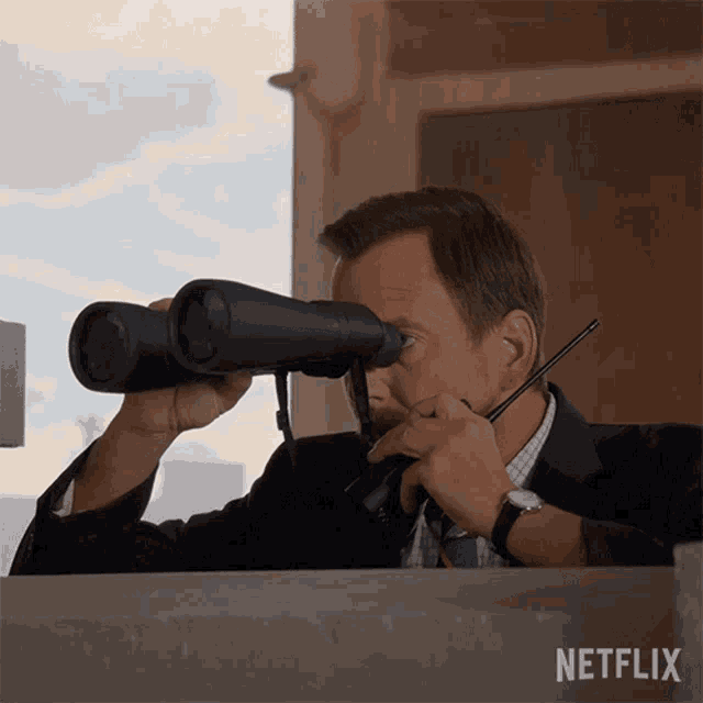 a man in a suit is looking through binoculars with a netflix logo behind him