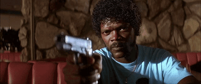 a man with curly hair and a mustache is pointing a gun at the camera