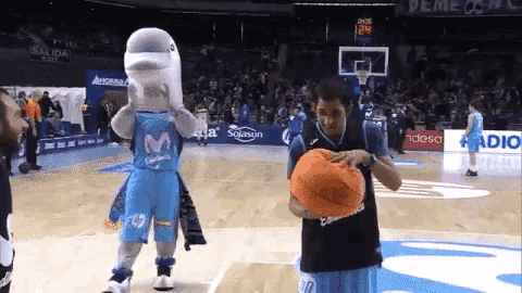 a man holding a basketball in front of a dolphin mascot