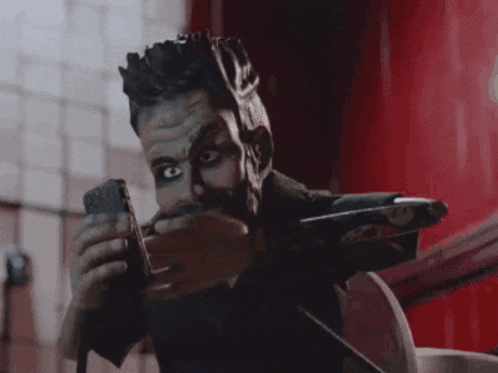 a man with black paint on his face is holding a cellphone