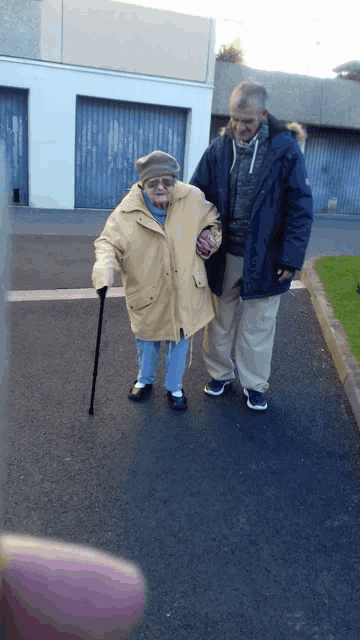 a man in a blue jacket helps an elderly woman walk down the street