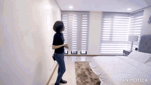 a woman is standing in a bedroom with a bed and a rug .