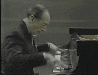 a man in a suit is playing a piano in a black and white photo .