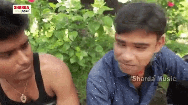 two men are sitting next to each other in a garden talking to each other .