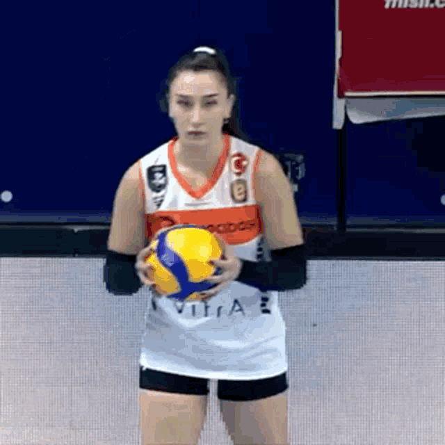 a female volleyball player is holding a yellow volleyball in her hands .