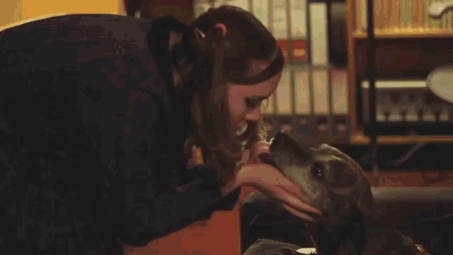 a woman petting a brown dog in front of a shelf of binders