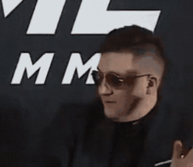 a man wearing sunglasses stands in front of a sign that says " mm "