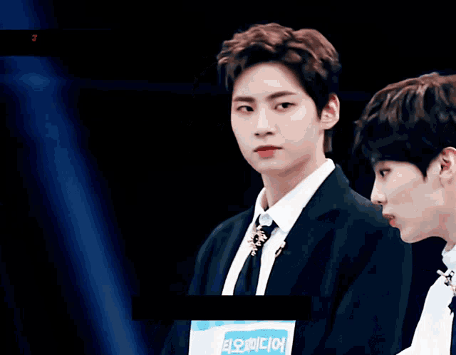 a man in a suit and tie stands next to another man in a white shirt and tie