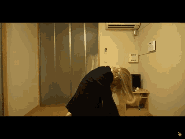 a woman in a black suit is bending over in a room with a computer on a desk