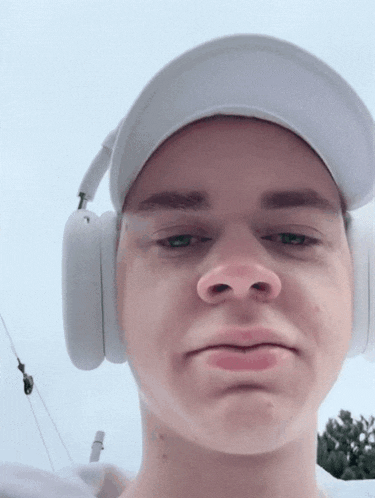 a young man wearing headphones and a hat is making a face