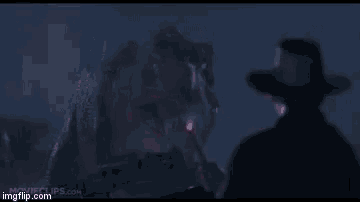 a man in a cowboy hat is standing in front of a t-rex in a movie .