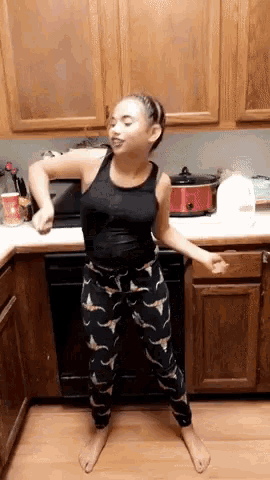 a young girl is dancing in a kitchen with a red crock pot in the background