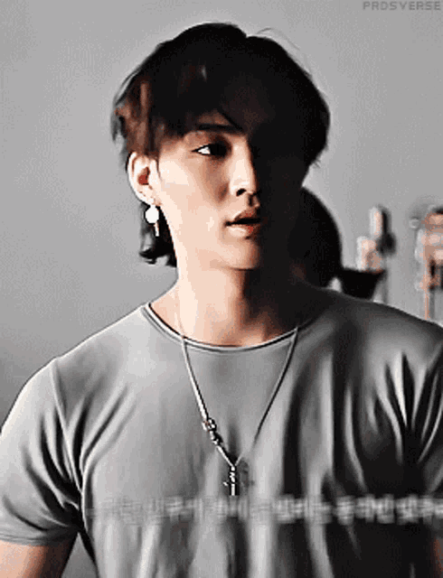 a young man wearing a gray shirt and a necklace with the word prosverse on the bottom right