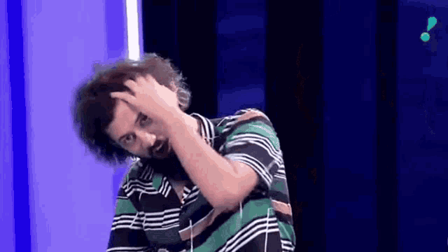a man with curly hair is scratching his head while wearing a green and white striped shirt .