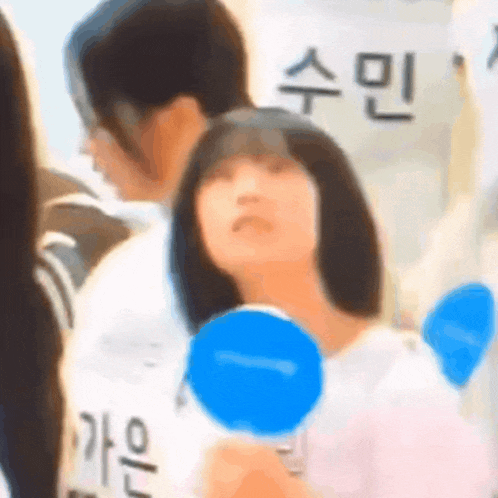 a girl is holding a blue object in her hand while standing in a crowd of people .