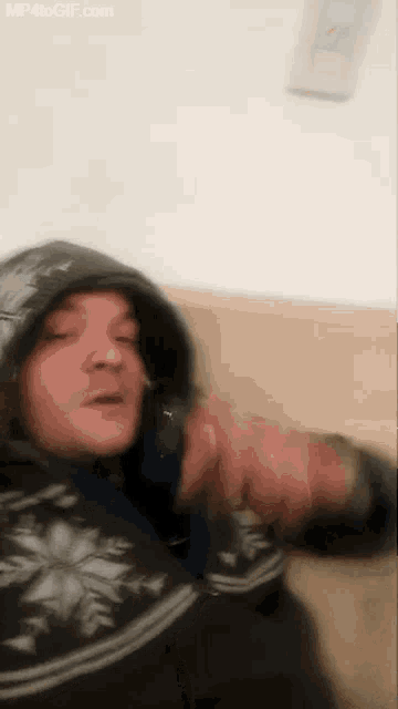 a man in a hooded jacket is laying on a couch and talking on a phone .