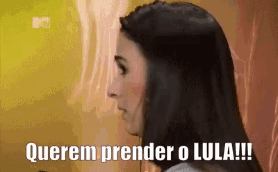 a woman with long dark hair is standing in front of a wall with the words querem prender o lula written on it .