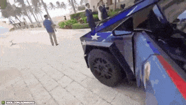 a blue car with a red white and blue stripe on the side is parked on a sidewalk .
