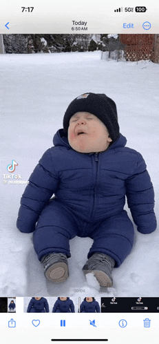 a baby in a blue jacket is sitting in the snow at 6:30 am