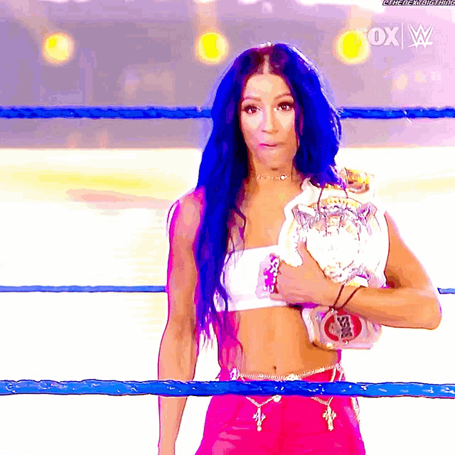 a woman with blue hair is standing in a ring holding a championship belt