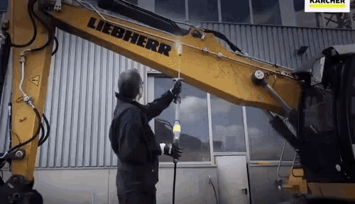 a man is cleaning a liebherr excavator with a spray gun