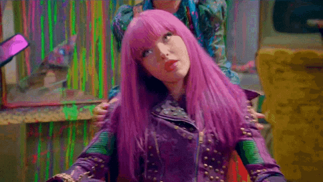 a girl with purple hair and a purple jacket is sitting in a chair .