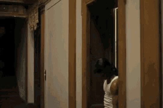 a man in a white tank top stands in a hallway between two doors