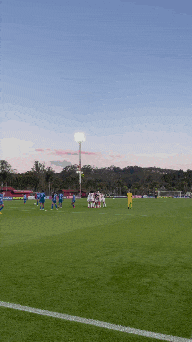 a group of soccer players on a field with a stadium in the background