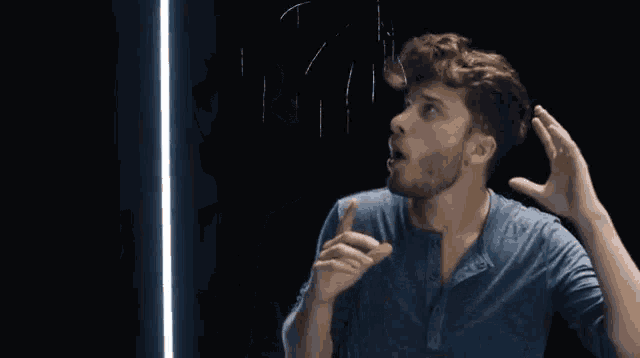 a man in a blue shirt looks up at something in the dark