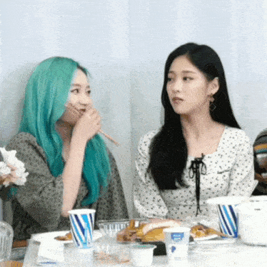 two women are sitting at a table with a cup that says ' yoghurt ' on it