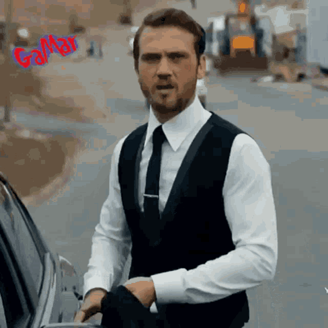 a man in a white shirt and black vest is standing next to a car