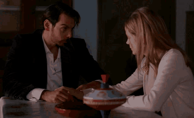 a man and a woman are sitting at a table looking at a spinning top